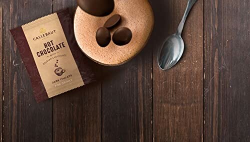 Beker warme chocolademelk met lepel en Callebaut chocolademelkverpakking op houten tafel.