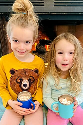 Twee kinderen drinken warme chocolademelk voor de open haard.