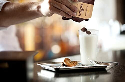 Hand voegt chocoladedruppels toe aan glas melk.